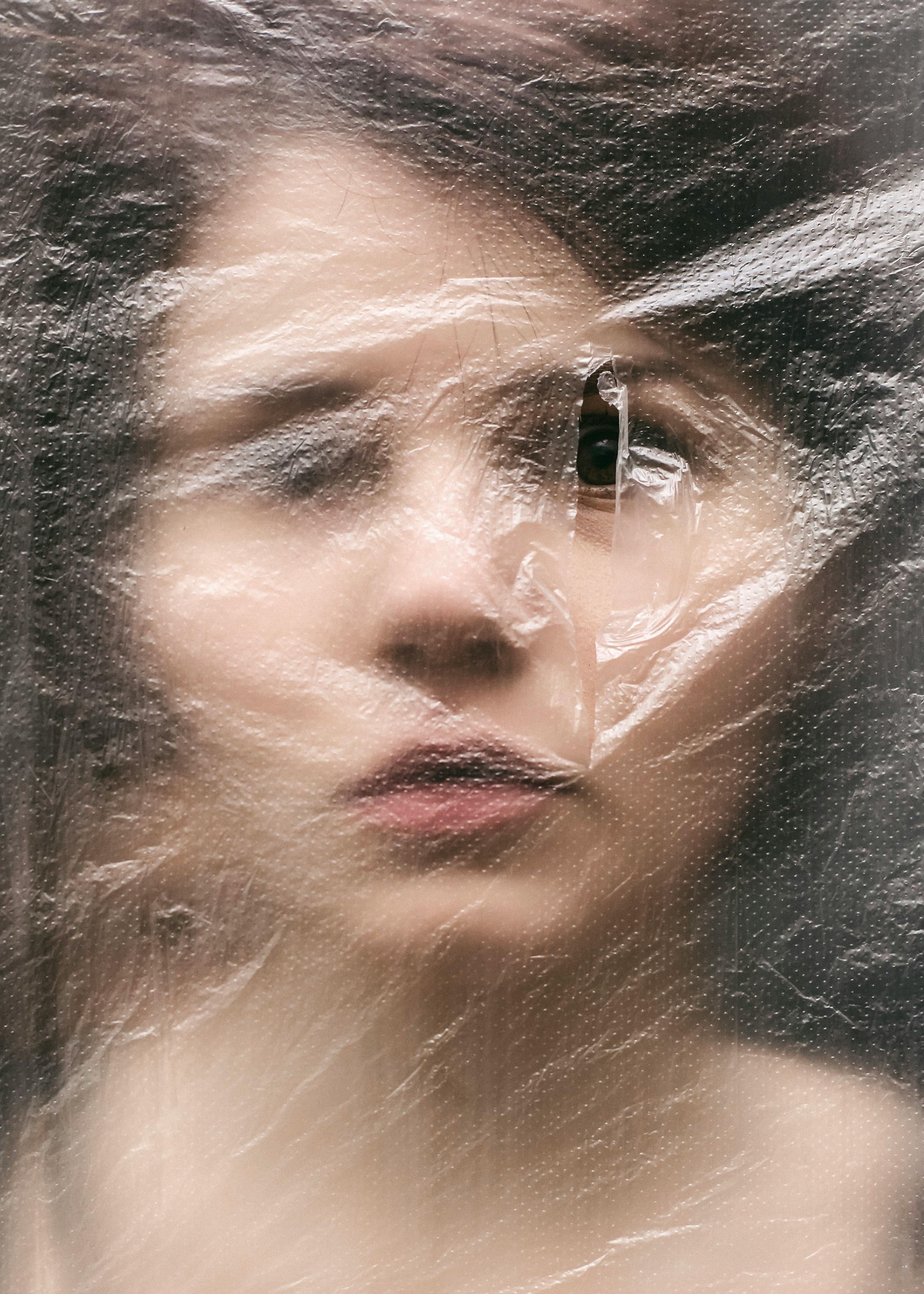 Close-up of a woman’s face partially obscured by stretched transparent plastic wrap